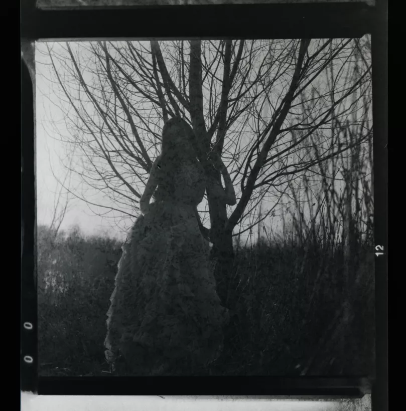 Analoges Schwarz-Weiß-Portrait einer Person in einem voluminösen Kleid vor einem kahlen Baum