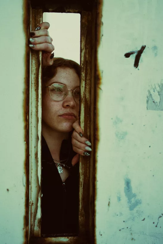 Künstlerisches Portrait einer Person mit Brille, die durch einen schmalen, rostigen Spalt blickt