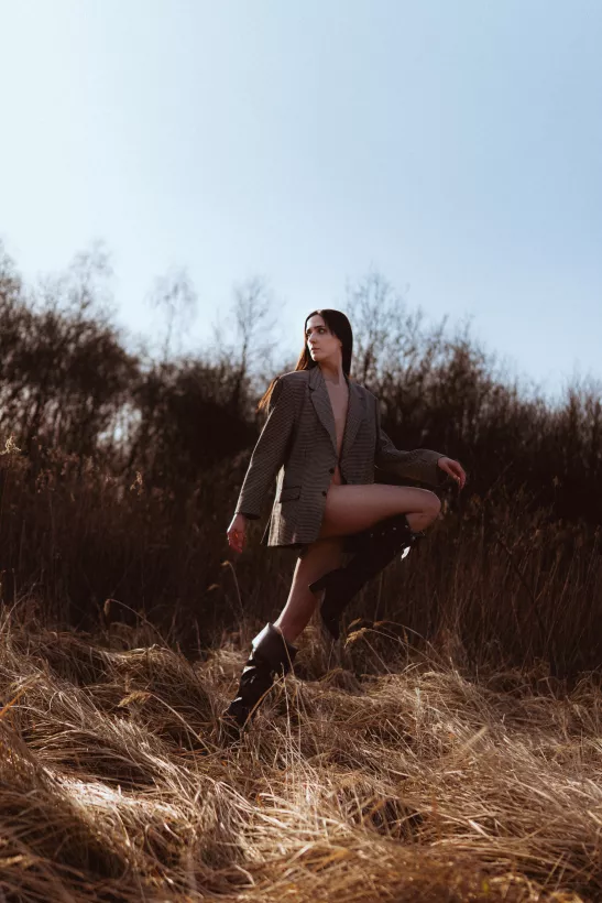 Fashion-Portrait einer Frau in kariertem Blazer und Stiefeln im hohen Gras
