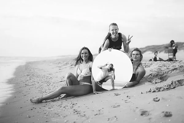 Künstlerisches Schwarz-Weiß-Gruppenfoto von drei Personen mit einem runden Spiegel am Strand
