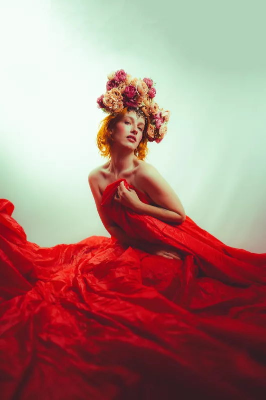 Studioportrait einer Frau mit opulentem Blumenkranz und fließendem roten Gewand