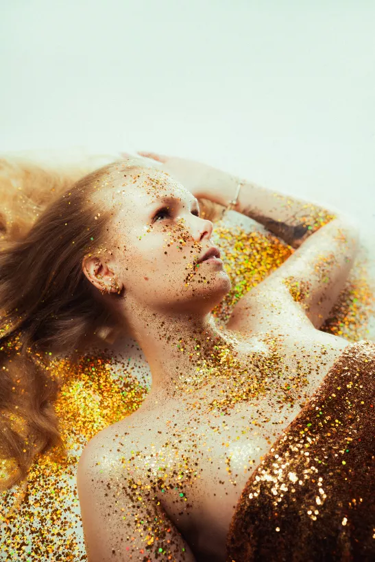 Künstlerisches Portrait einer blonden Frau mit goldenem Glitzer auf der Haut