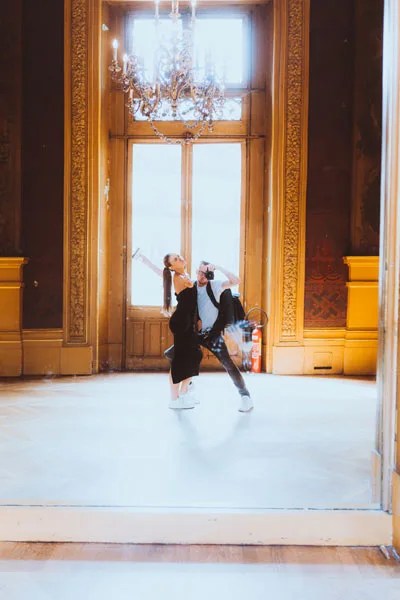 Ein Paar in dynamischer Pose in einem prunkvollen Saal mit Kronleuchter.