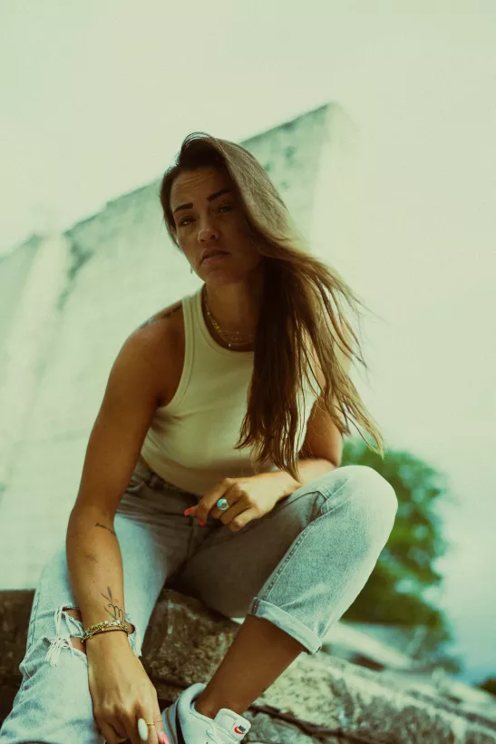 Portrait einer Frau in weißem Tanktop und heller Jeans auf einer Betonstruktur